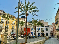 Sunny day in Alicante featuring coastal views, palm-lined promenades, and colorful Spanish architecture with the Santa Bárbara Castle in the background.