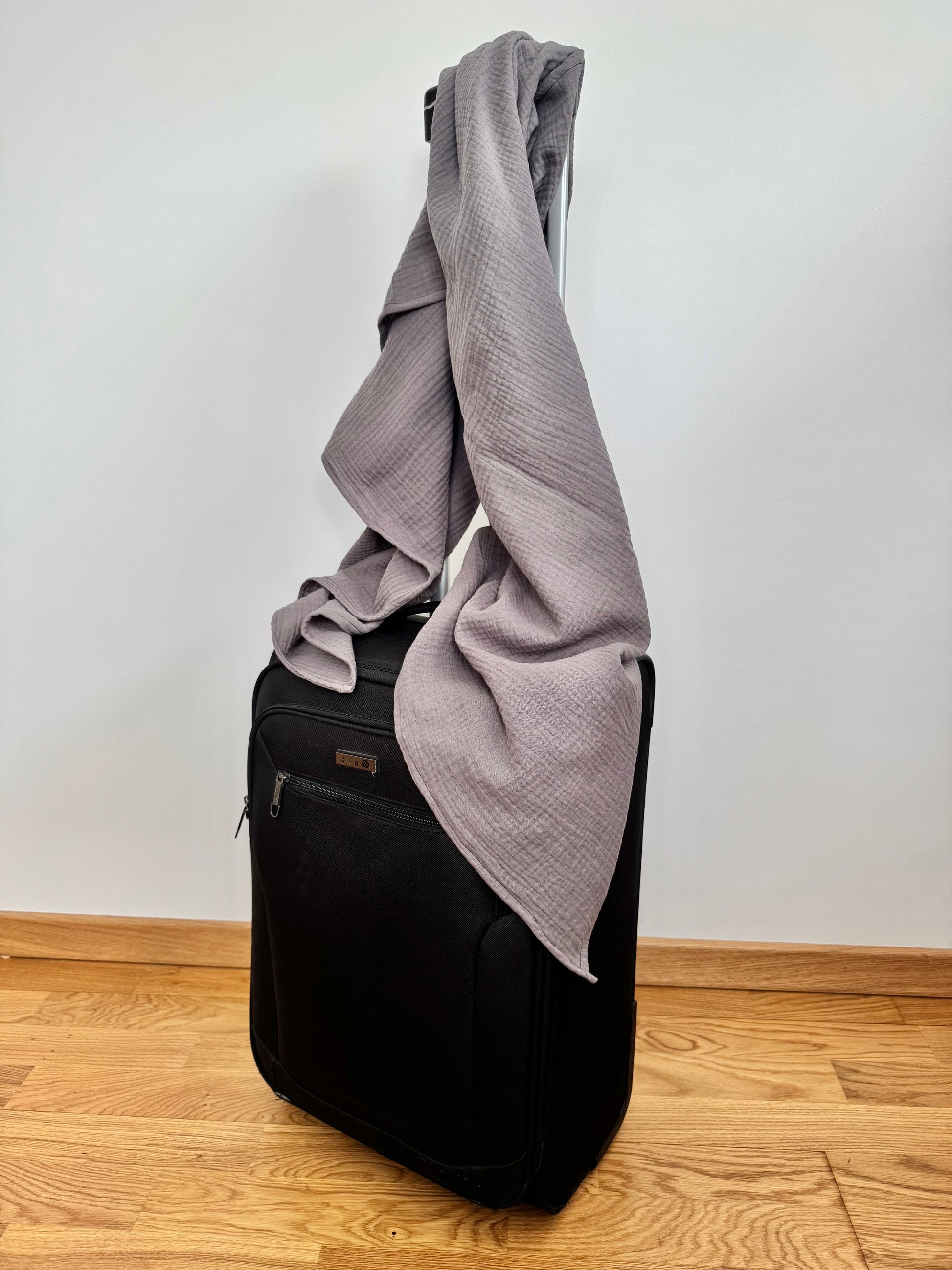 Black suitcase with a gray scarf draped over it on a wooden floor.